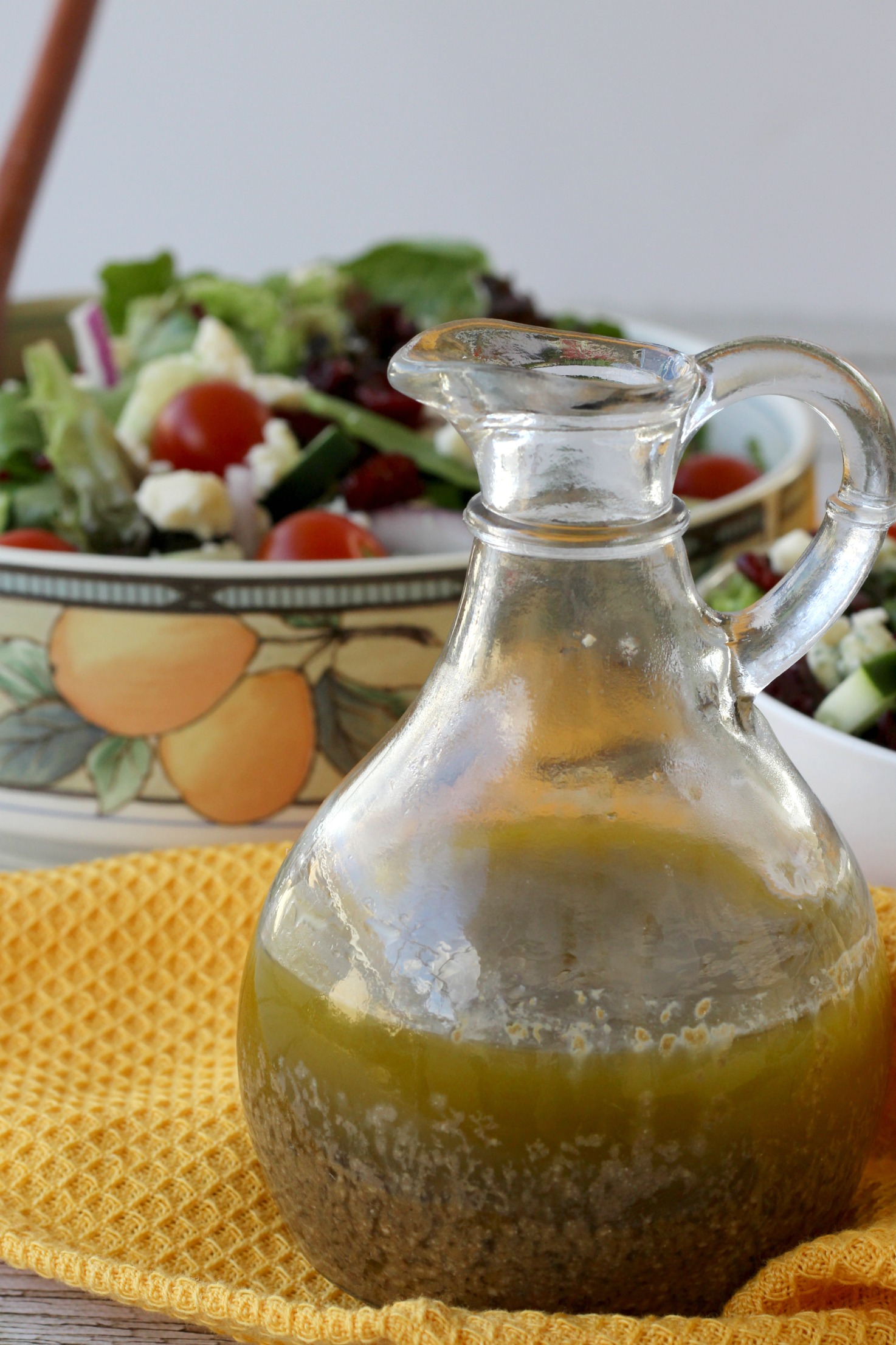 A pitcher of blue cheese dressing on a table next to a salad.