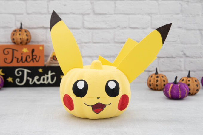 A cute pikachu pumpkin sitting on a table next to Halloween decorations.