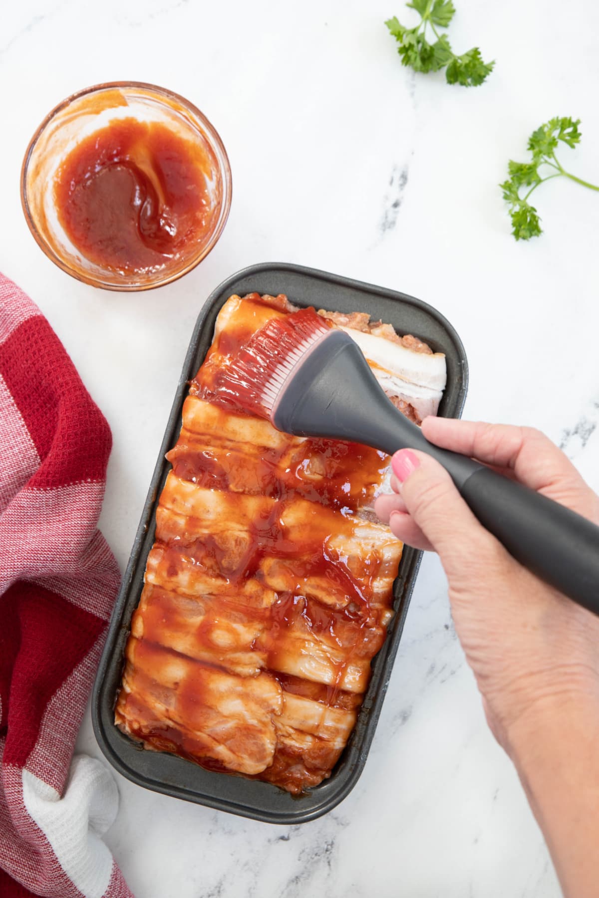 Brushing ketchup glaze over meatloaf wrapped with bacon