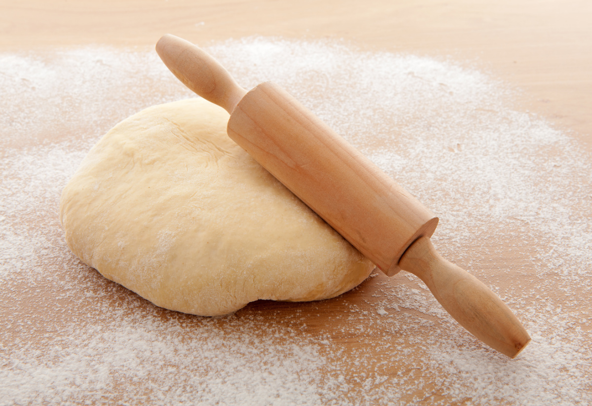 A wooden rolling pin on top of a pizza dough.