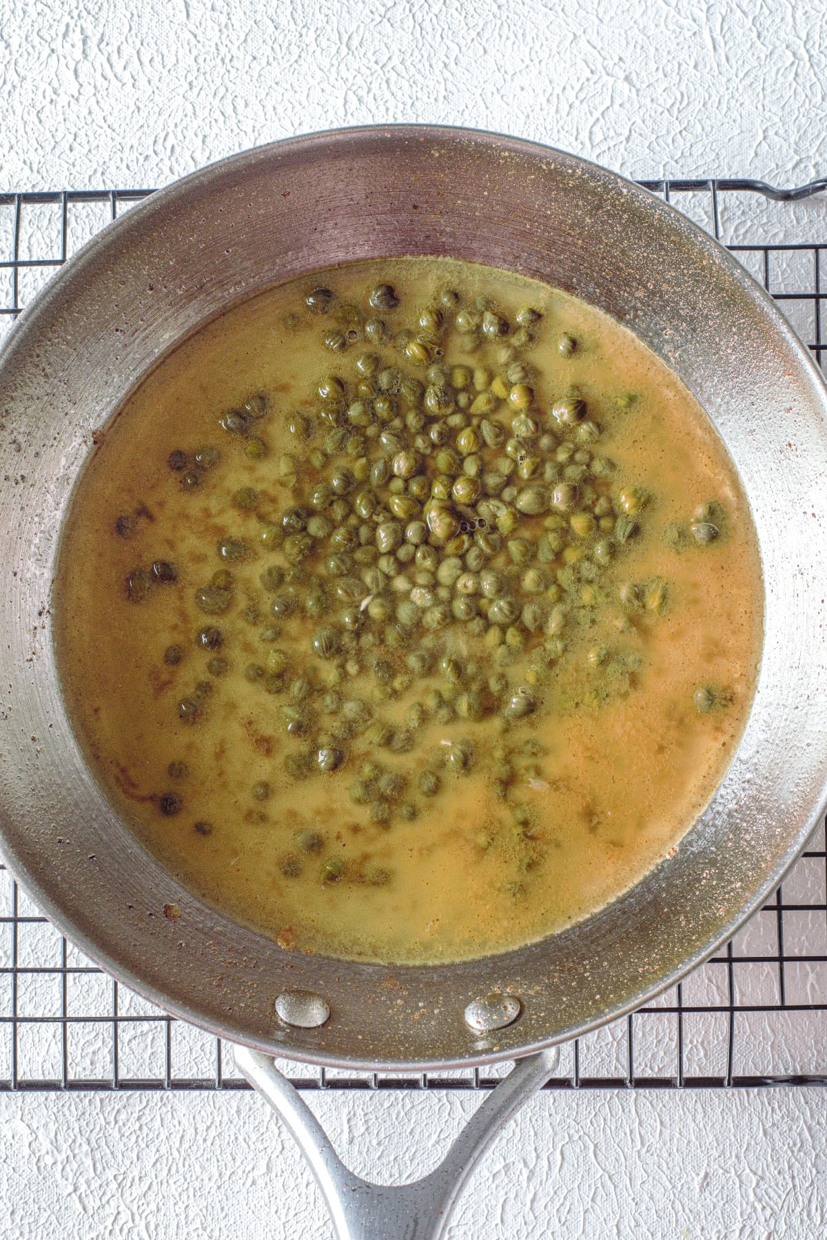 Capers in pan with chicken stock and lemon juice