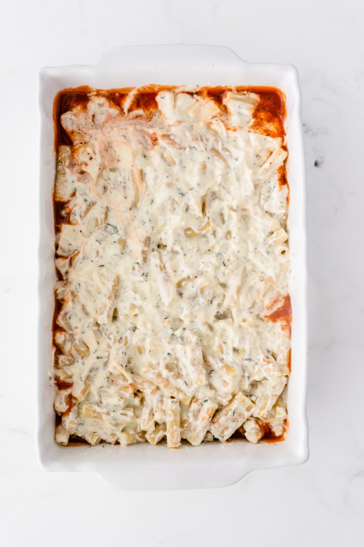 Layers of tomato sauce, pasta and cheese sauce in pan