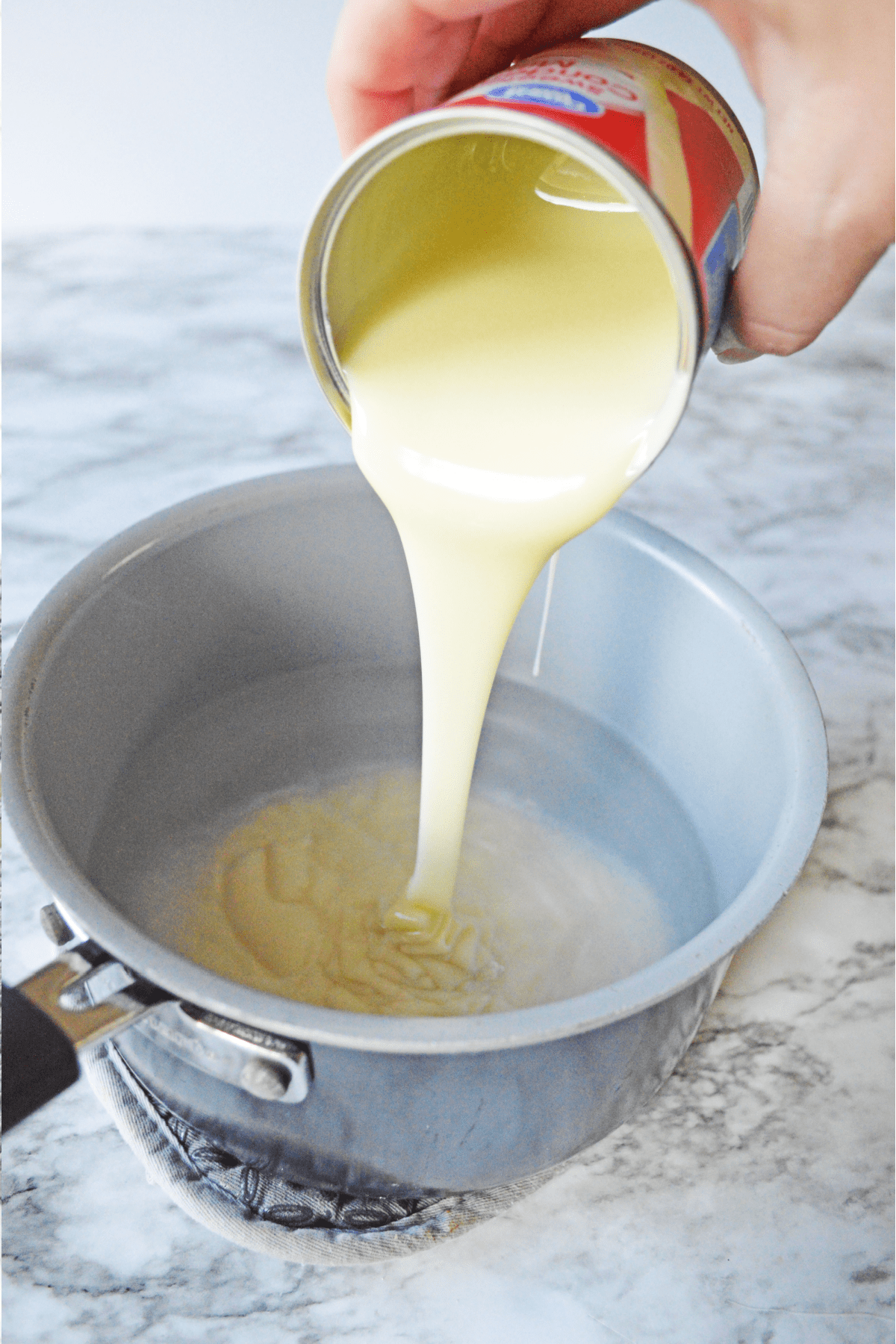 Pouring condensed milk into a saucepan of water