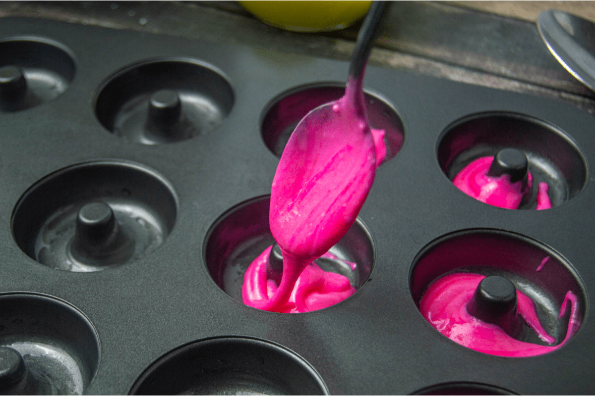 Pink donut batter being spooned into doughnut pan