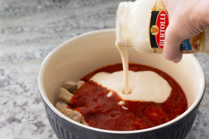 Pouring alfredo sauce into chicken pasta mixture