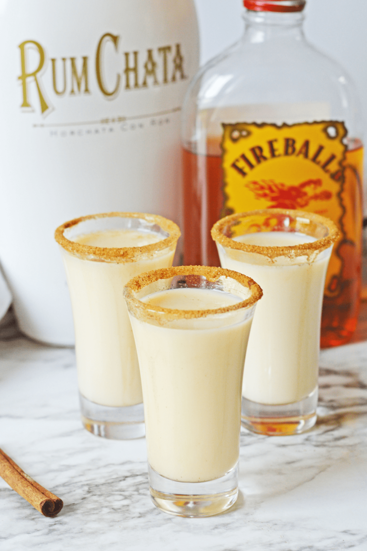 Three Cinnamon Toast Crunch Shots with alcohol behind