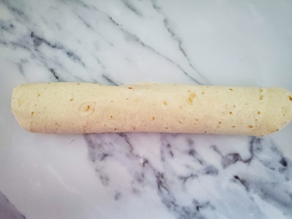 Tortilla filled with cream cheese mixture rolled up on counter
