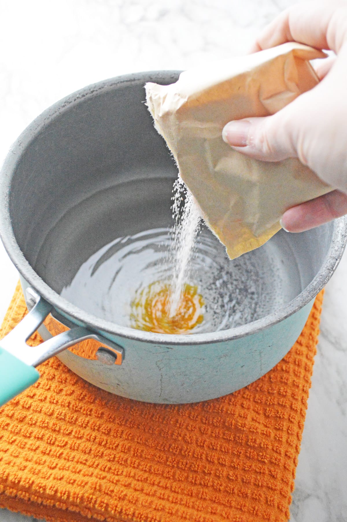 Pouring orange jello mix into saucepan with water