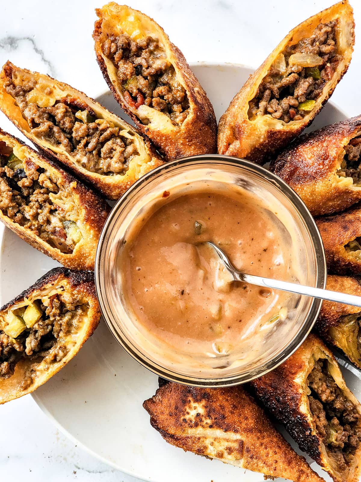 Cheeseburger egg rolls placed around dipping sauce