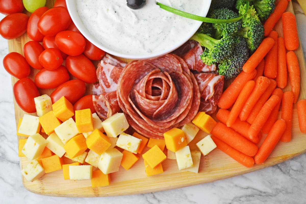 Veggies and cheese chunks on wooden board with dip