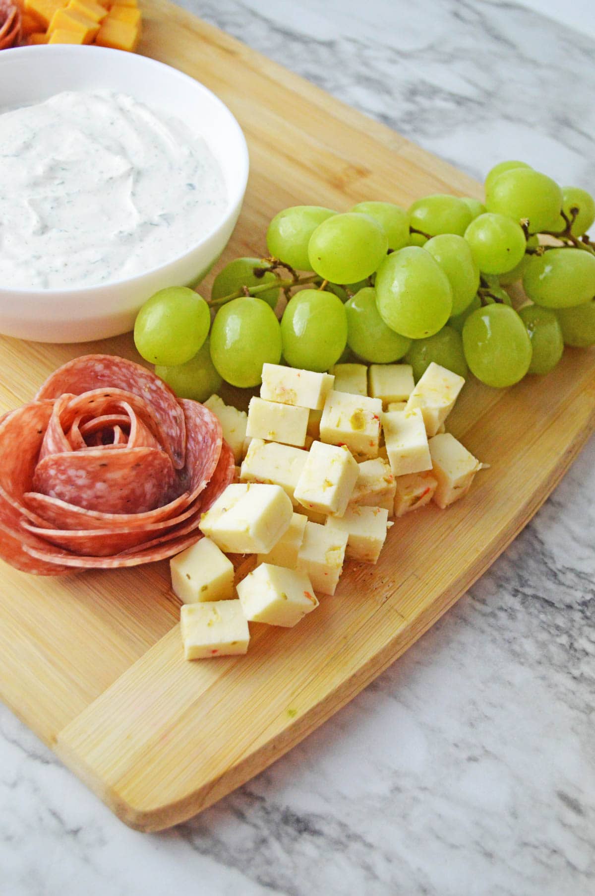 Cheese added to cutting board with fruit and meat