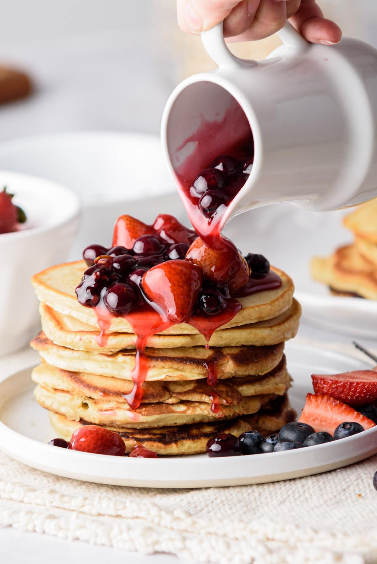 Berry syrup being poured over pancakes