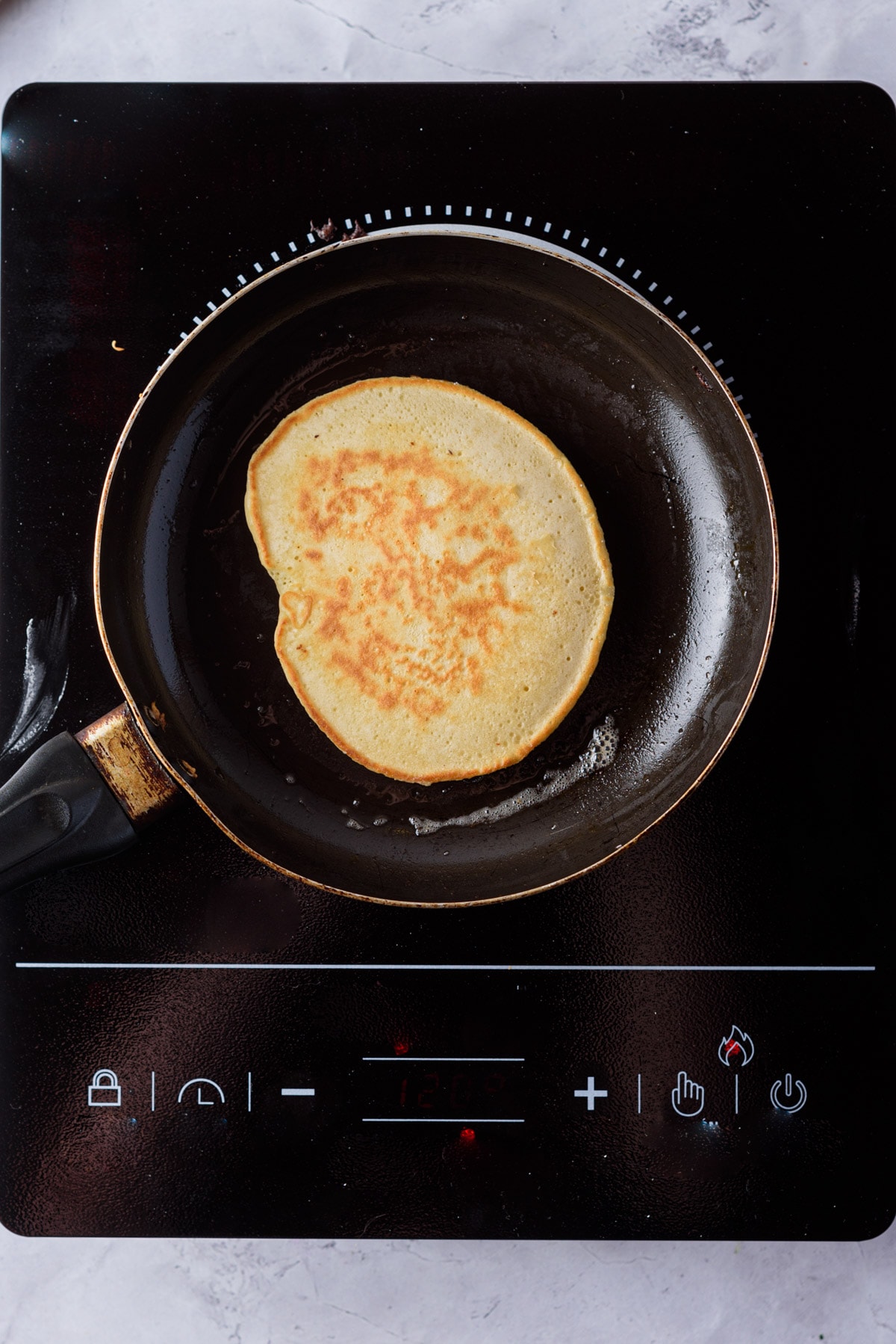 Pancake cooking in skillet with cooked side up