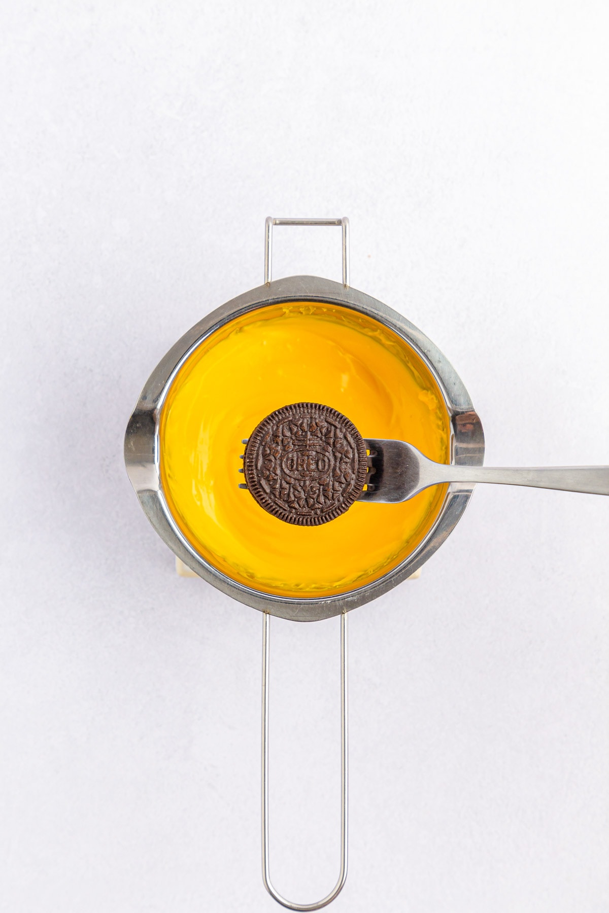 Oreo on a fork above a saucepan with yellow melted chocolate