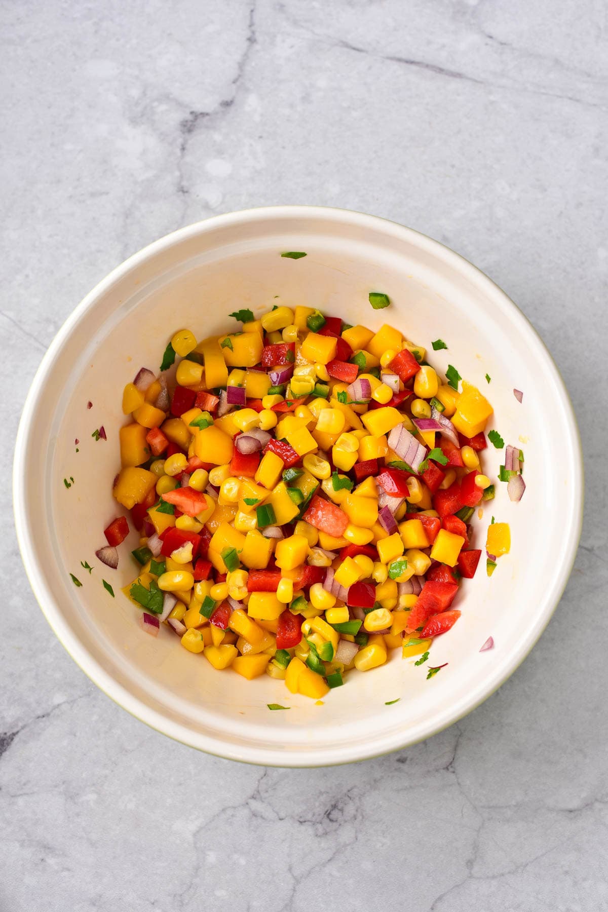 Ingredients for mango corn salsa mixed together in white bowl