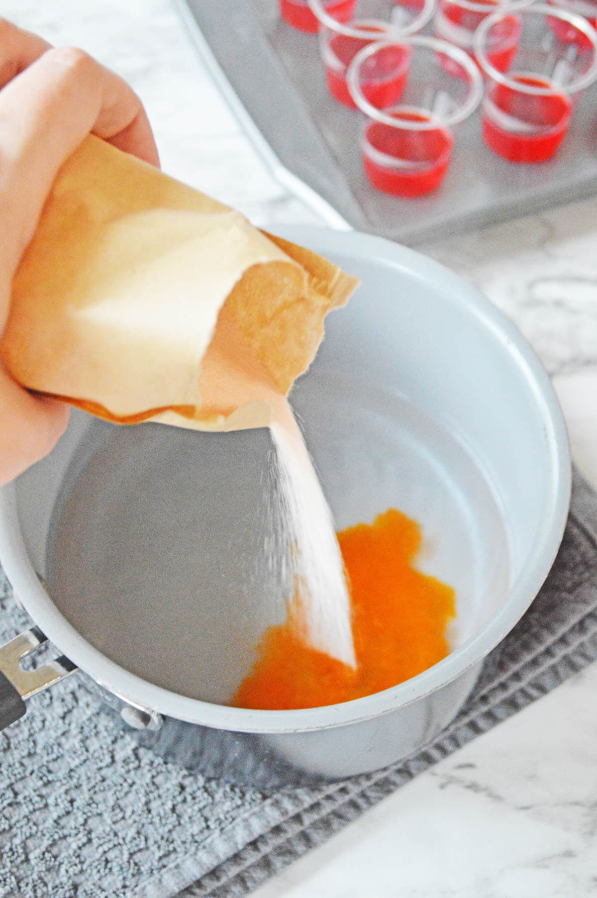 Pouring orange jello into water in saucepan