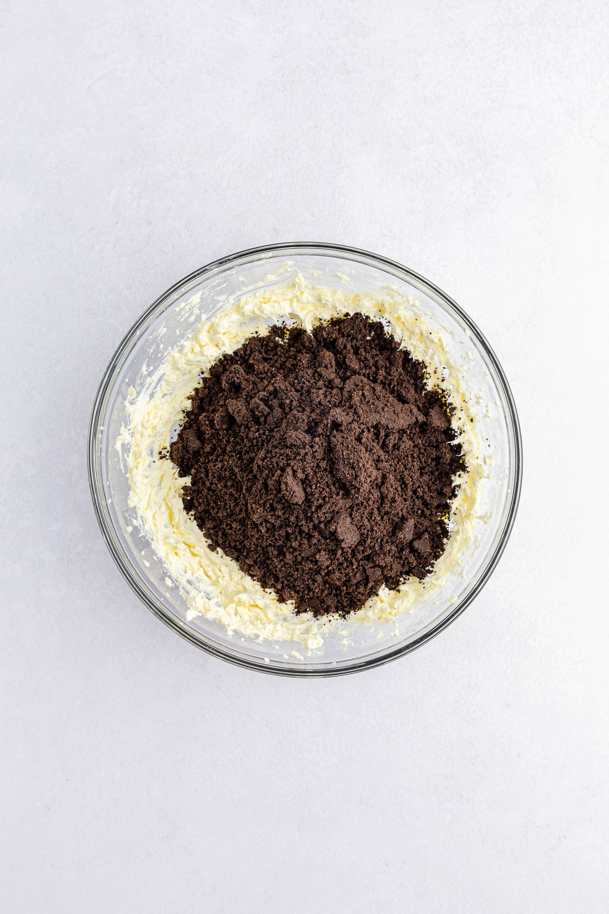 Cream cheese and Oreo cookie crumbs in glass mixing bowl