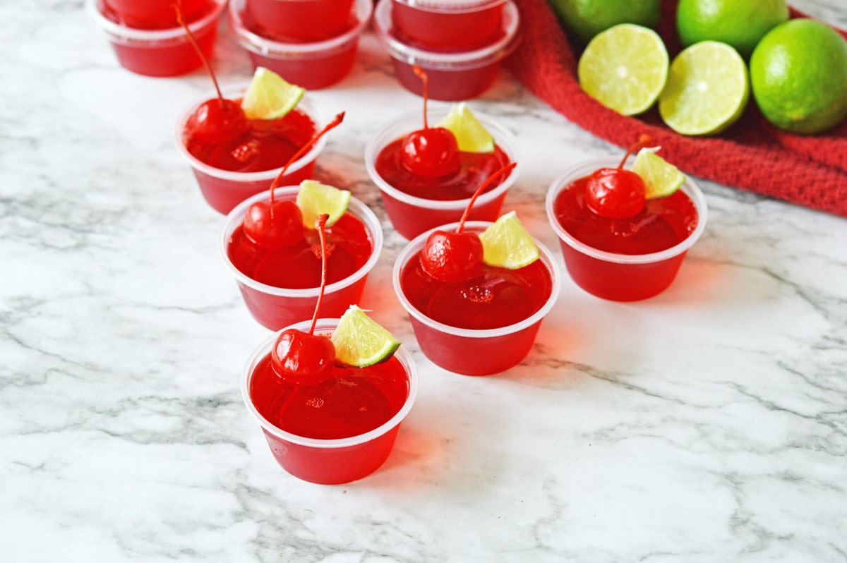 Cherry Limeade Jello shots on marble counter with limes and red towel