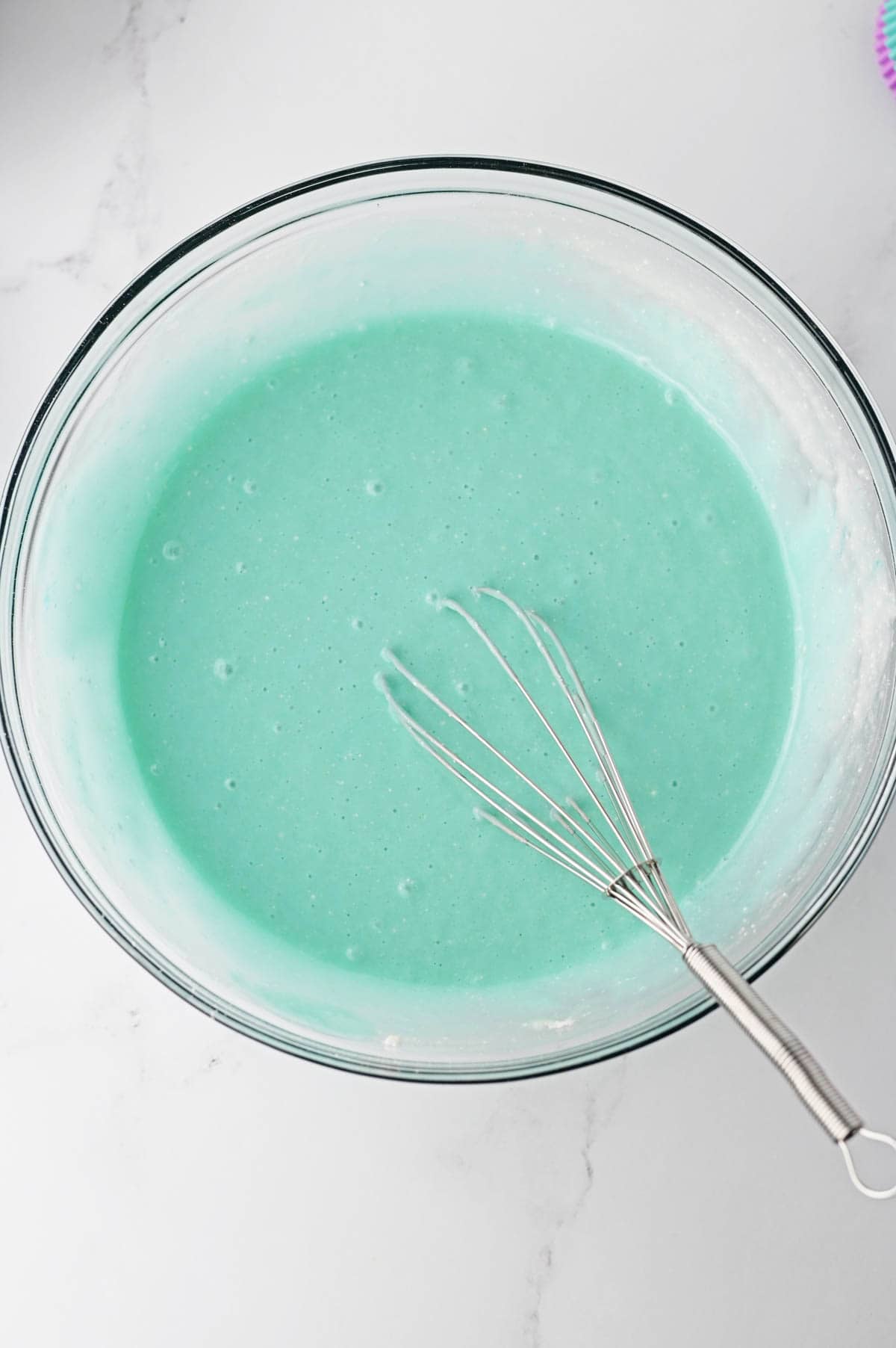 Cake batter with blue food coloring in glass bowl