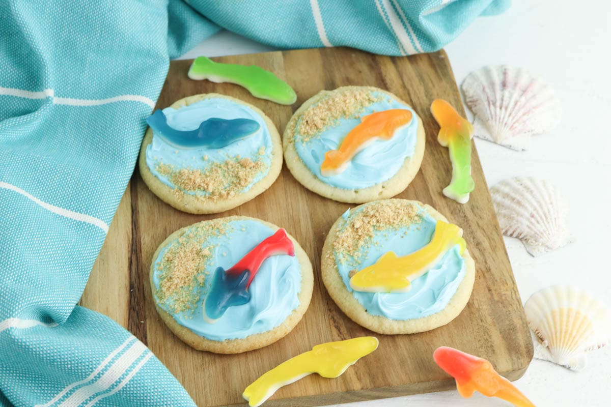 Sugar cookies with blue icing and sharks on wooden cutting board