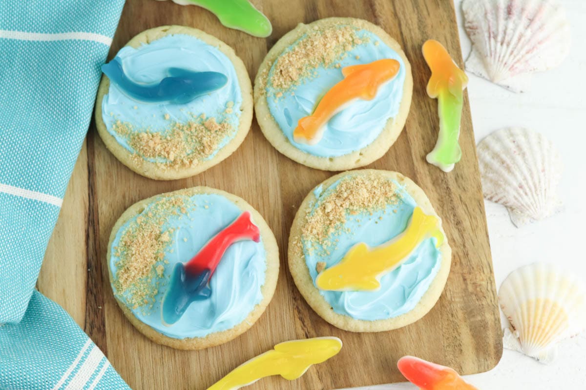 Shark cookies with gummy shark and graham cracker sand on wooden board