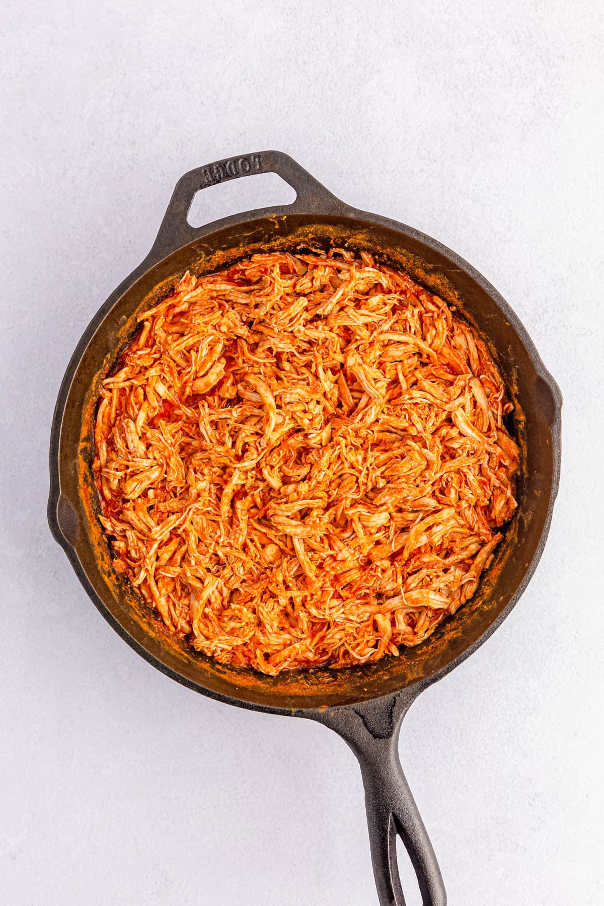 Shredded chicken mixed with hot sauce in iron skillet
