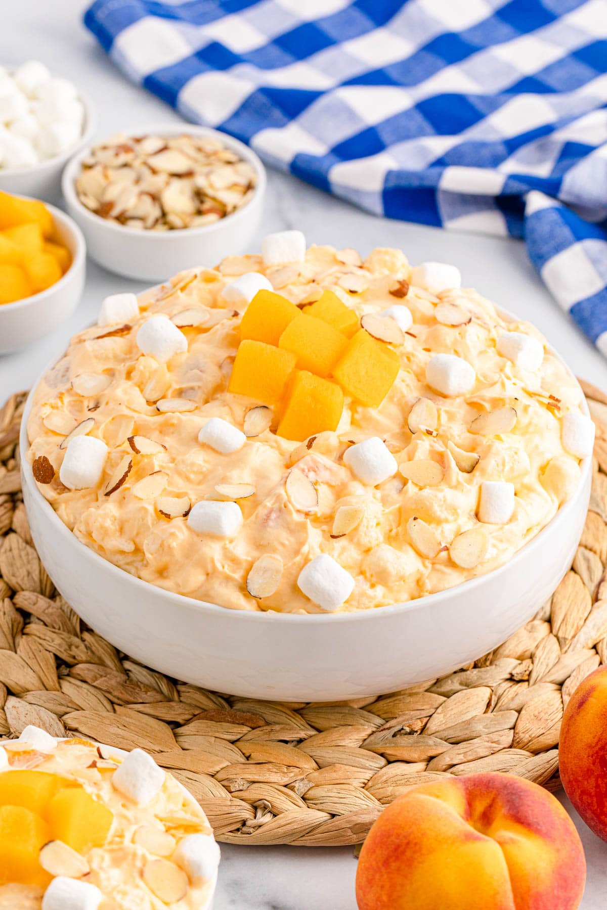 Bowl of peach fluff on a woven mat with blue checkered napkin with fresh peaches