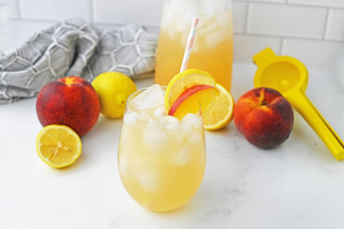 Peach lemonade in front of carafe with fresh lemons and peaches
