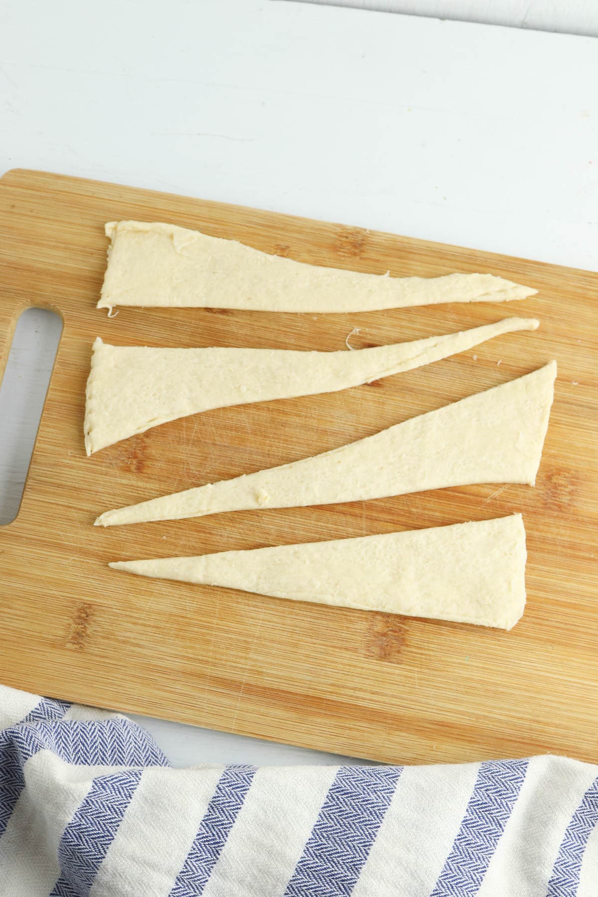Crescent rolls cut in half lengthwise on wooden board