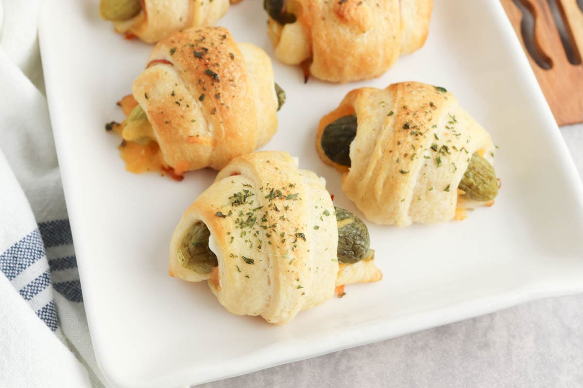 Pickles wrapped in crescent rolls on white plate with blue striped napkin