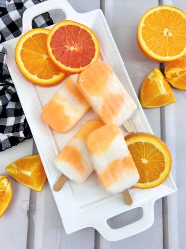 Boozy Orange Creamsicle Popsicles on white platter with black and white checkered napkin