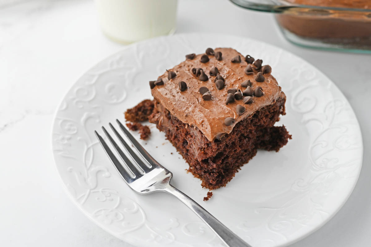Piece of chocolate poke cake on white plate with fork