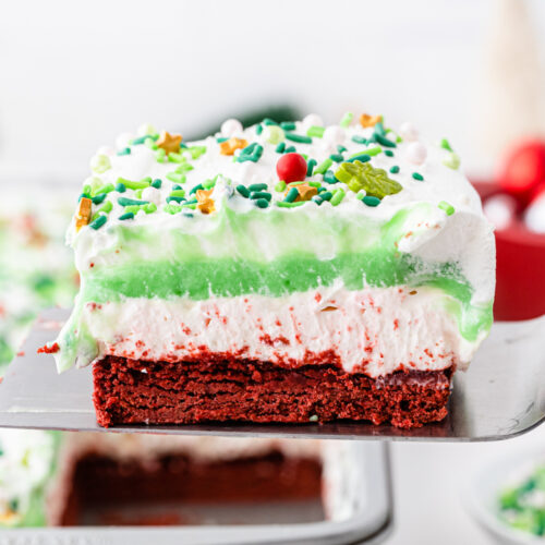 A slice of red velvet cake with green frosting and sprinkles.