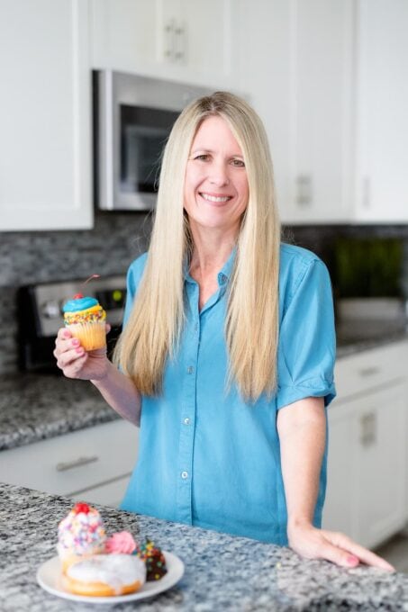 Lisa, author of Fun Money Mom, standing in front of a kitchen counter with a plate of donuts.