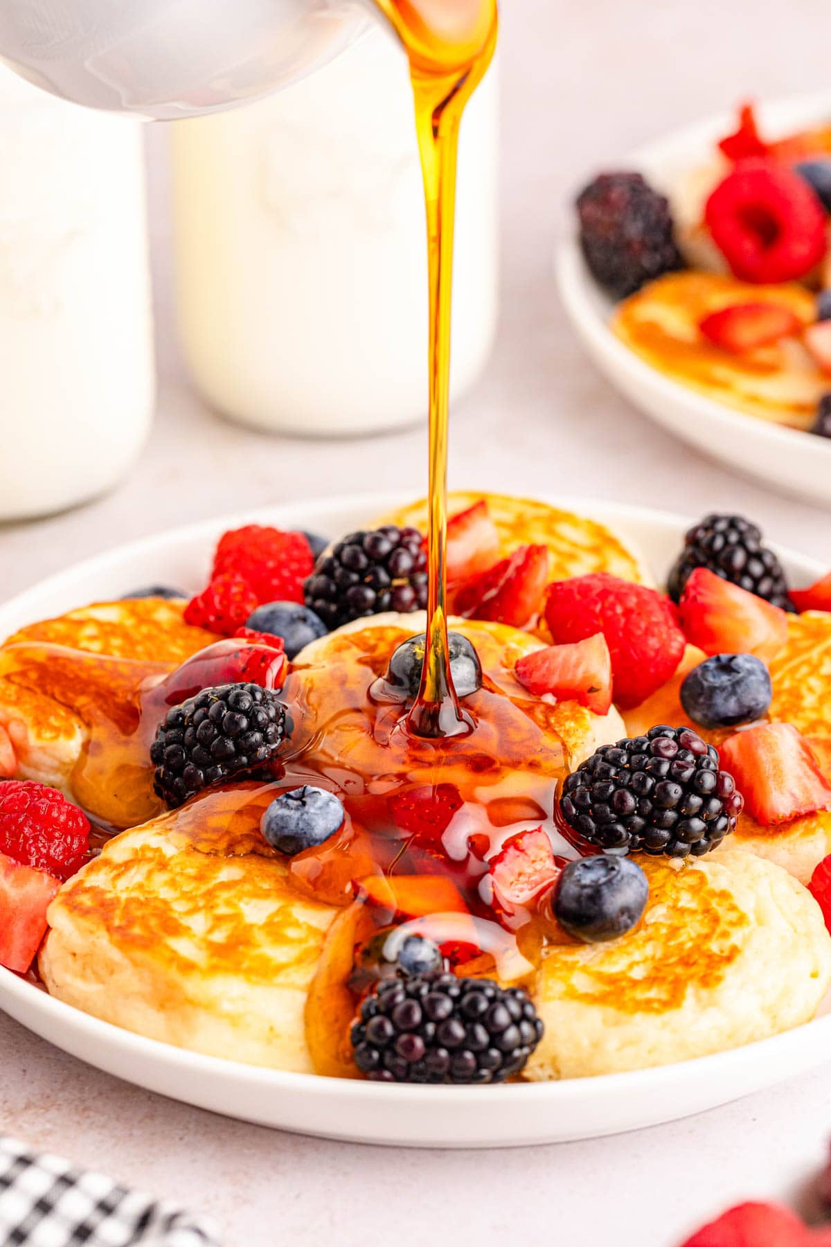 Pancakes with berries and syrup being poured over them.