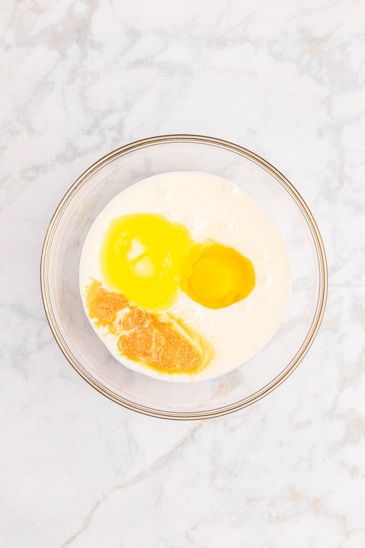 Two eggs, buttermilk and other wet ingredients in a bowl on a marble surface.