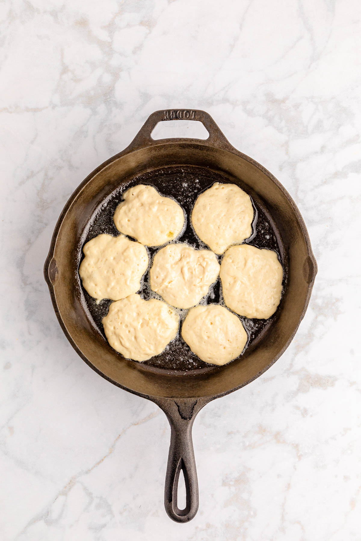 Fried biscuits in a skillet on a marble countertop.
