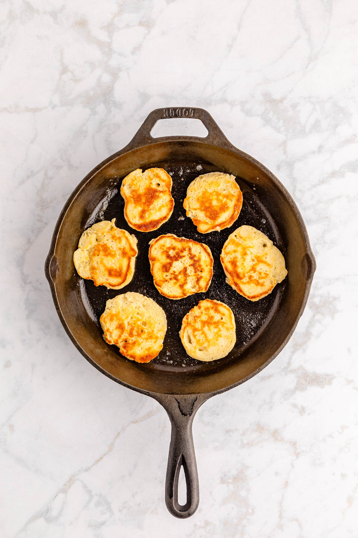 Pancakes in a cast iron skillet on a marble countertop.