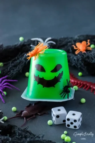 A green halloween jello cup with spiders and dice.