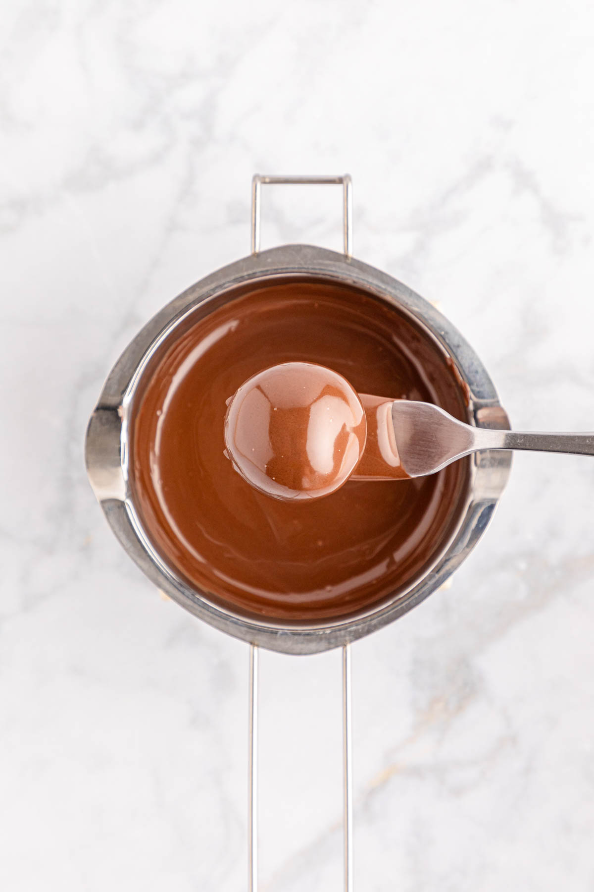 Chocolate sauce in a metal bowl with a chocolate ball on fork