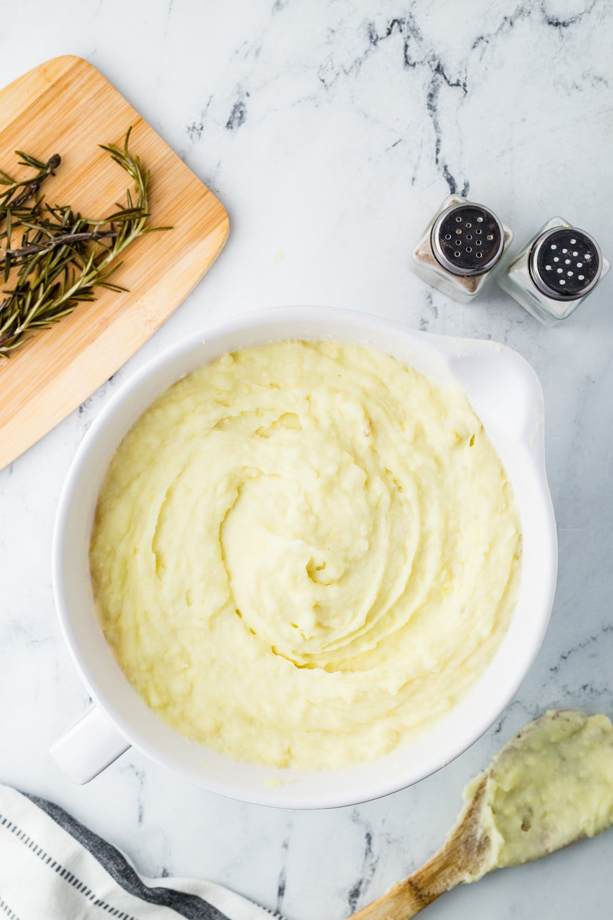 Mashed potatoes in a white bowl with sprigs of rosemary.