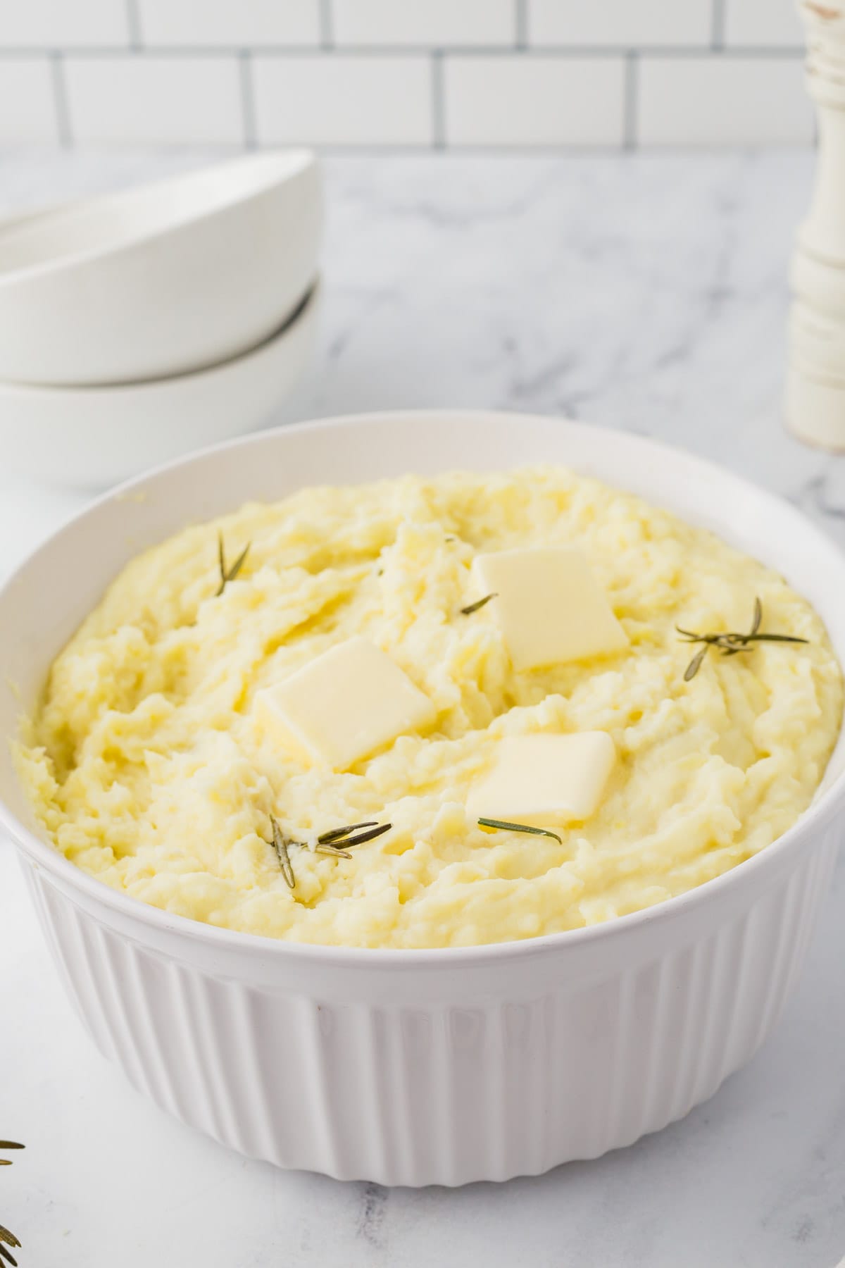 Mashed potatoes in a white bowl with butter and rosemary.