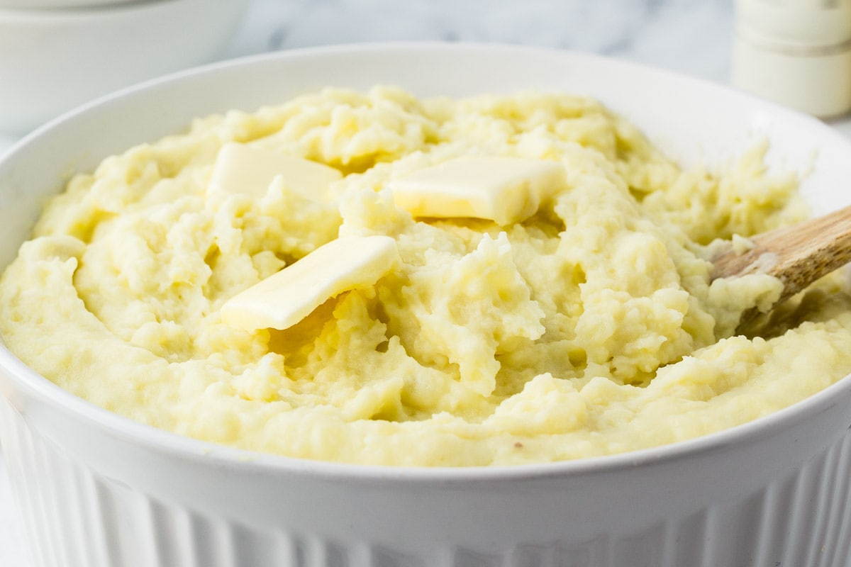 Mashed potatoes in a white bowl with a wooden spoon.