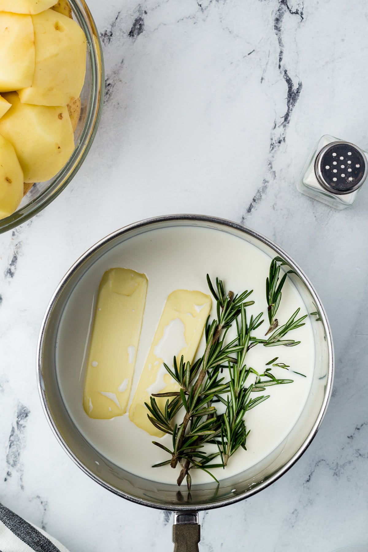 A pan with butter, rosemary, and cream on a marble countertop.