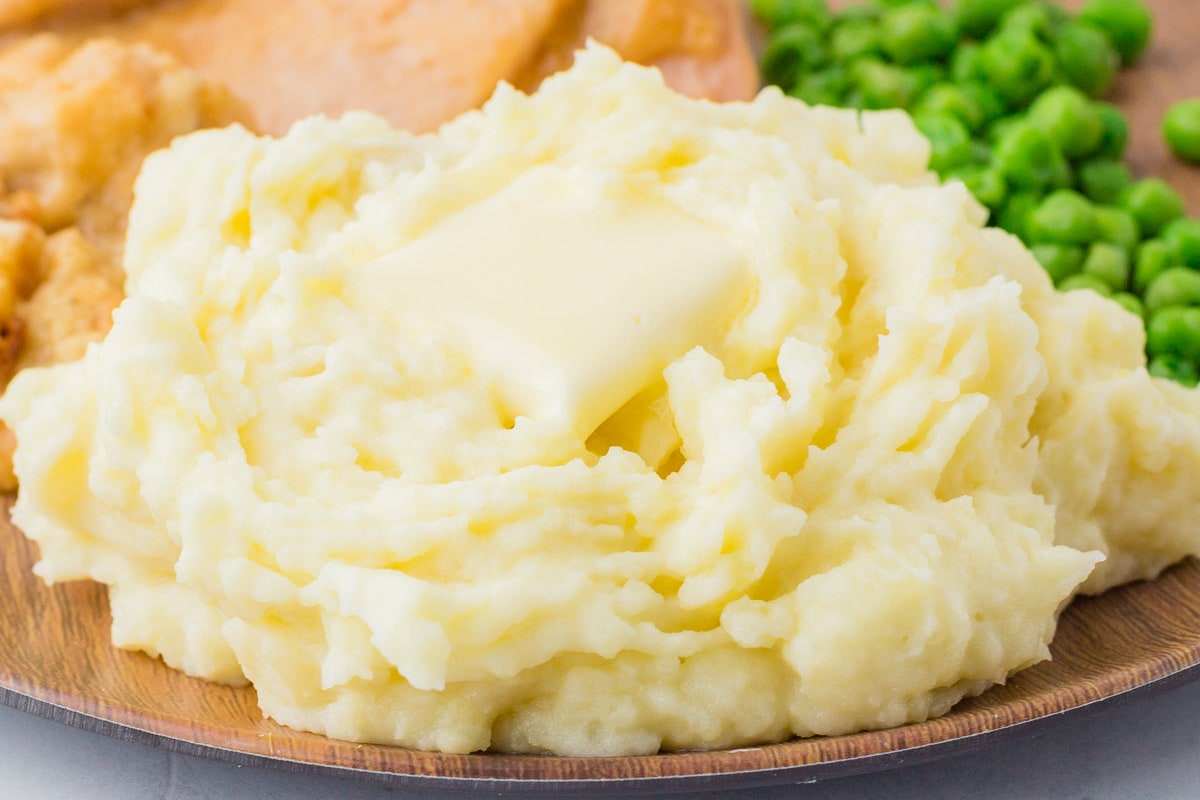 Mashed potatoes and peas on a wooden plate.