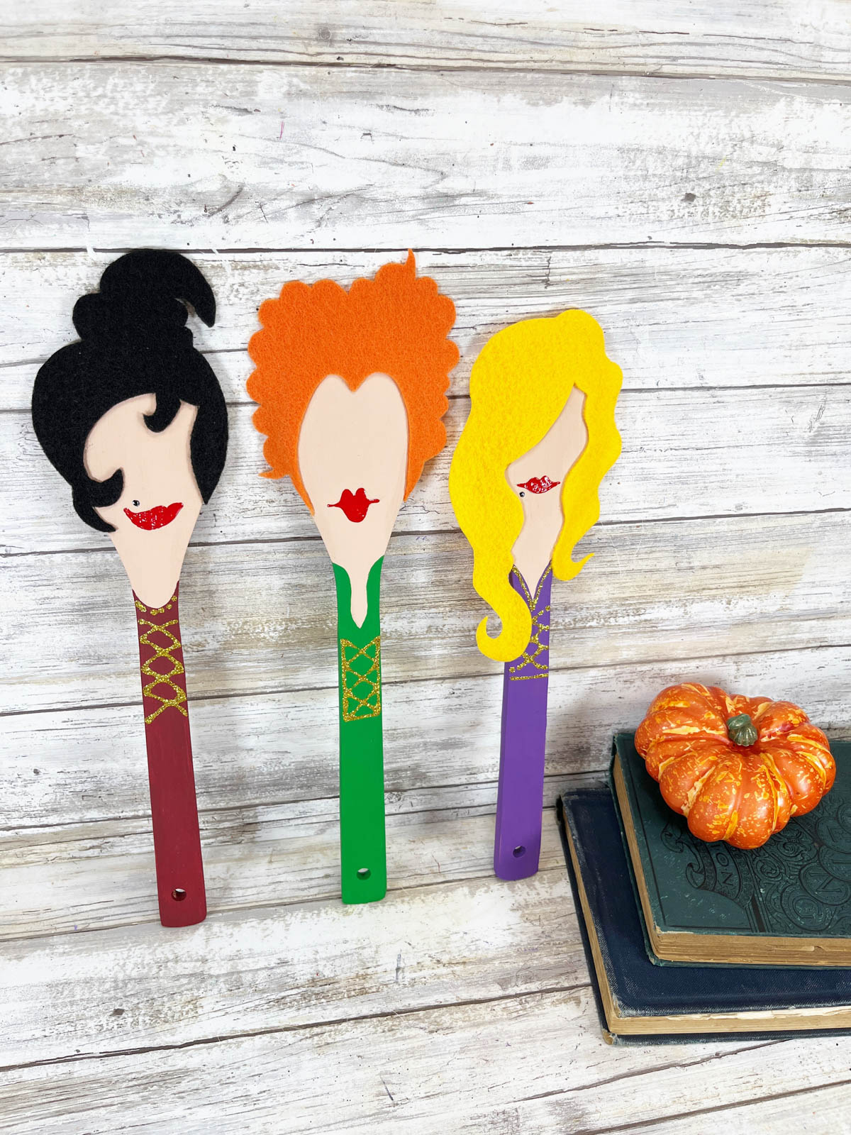 Three witches' spoons on a table next to pumpkins.