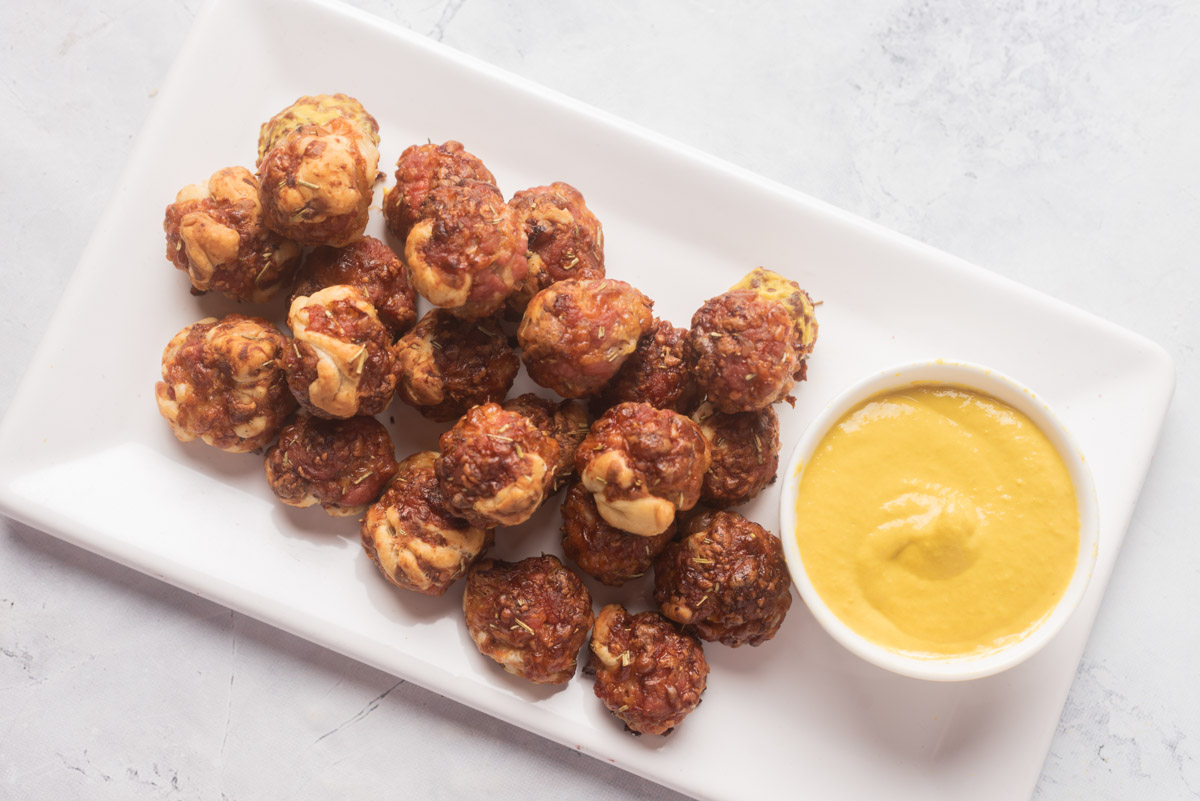 Sausage bites with mustard sauce on a white plate.