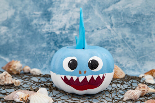 Shark painted pumpkin on top of fishing net with shells
