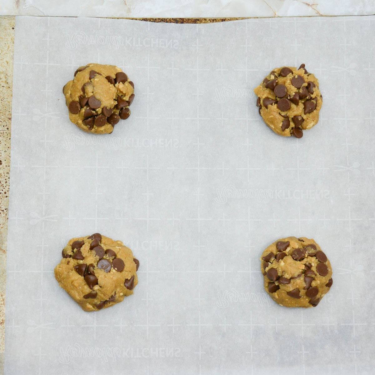 Four chocolate chip cookies on a baking sheet.