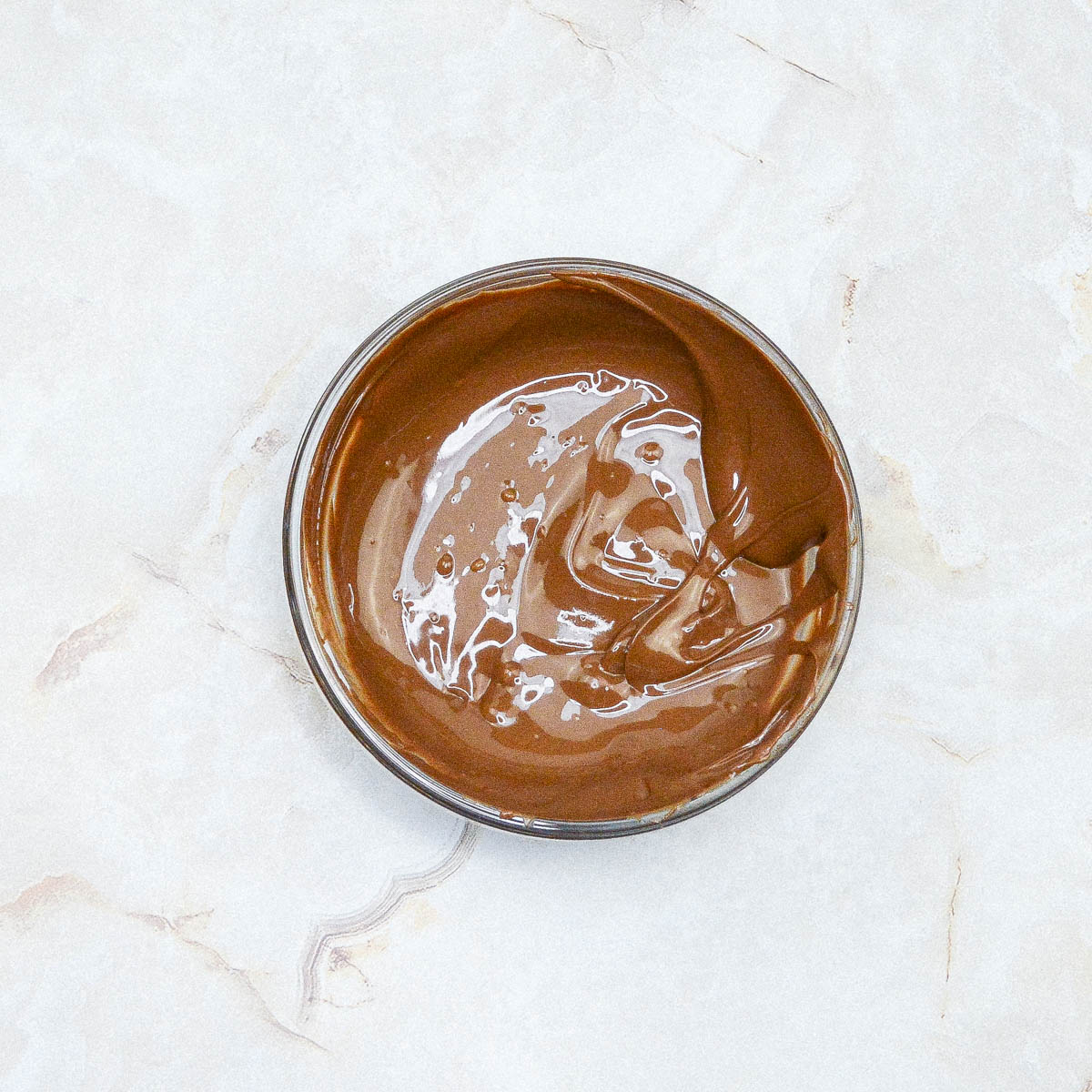 A bowl of chocolate on a marble surface.
